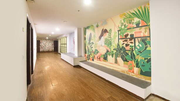 A hallway with wooden flooring, a large botanical mural on the right wall, and a door at the end. - Fabhotel Crescent (Faridabad)