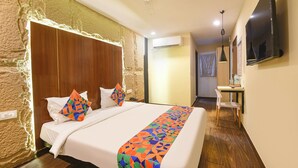 A hotel room with a large bed, a wooden headboard, a desk with a chair, a television, and a ceiling fan. - Fabhotel Crescent (Faridabad)
