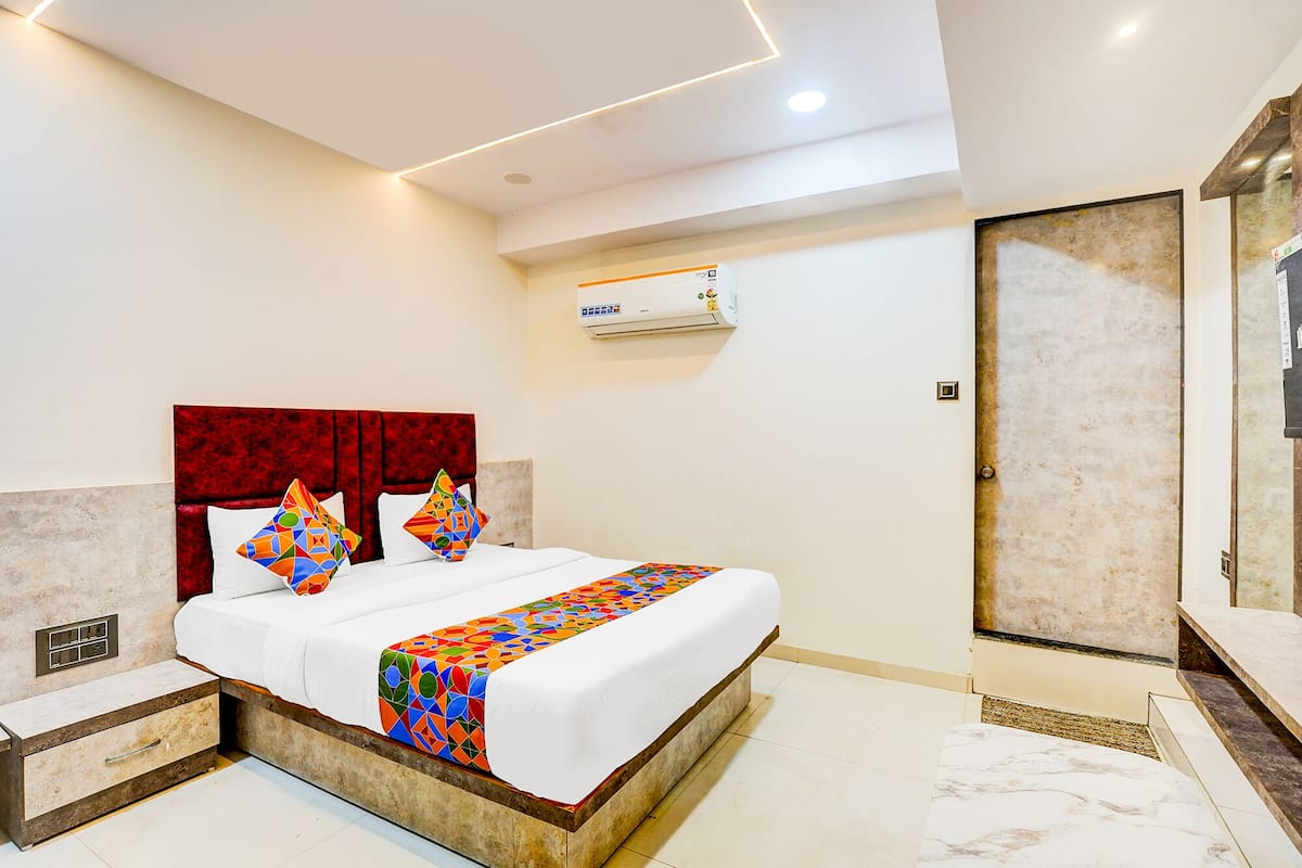 A modern hotel room with a large bed, a red headboard, a white bedside table, a built-in nightstand, a marble floor, a wall-mounted air conditioner, and a door with a textured finish.