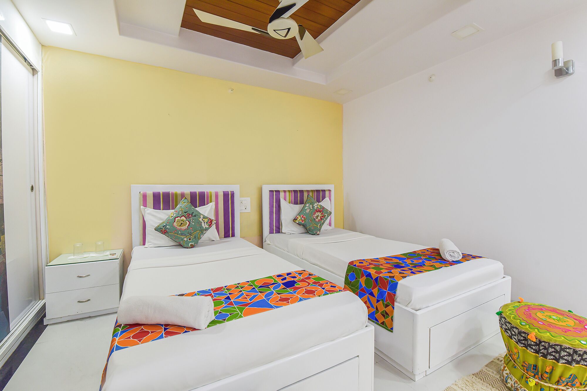 Une chambre d’hôtel avec deux lits, chacun agrémenté d’une couvre-lit colorée et d’oreillers à rayures. On y trouve une petite table avec une lampe et une chaise.