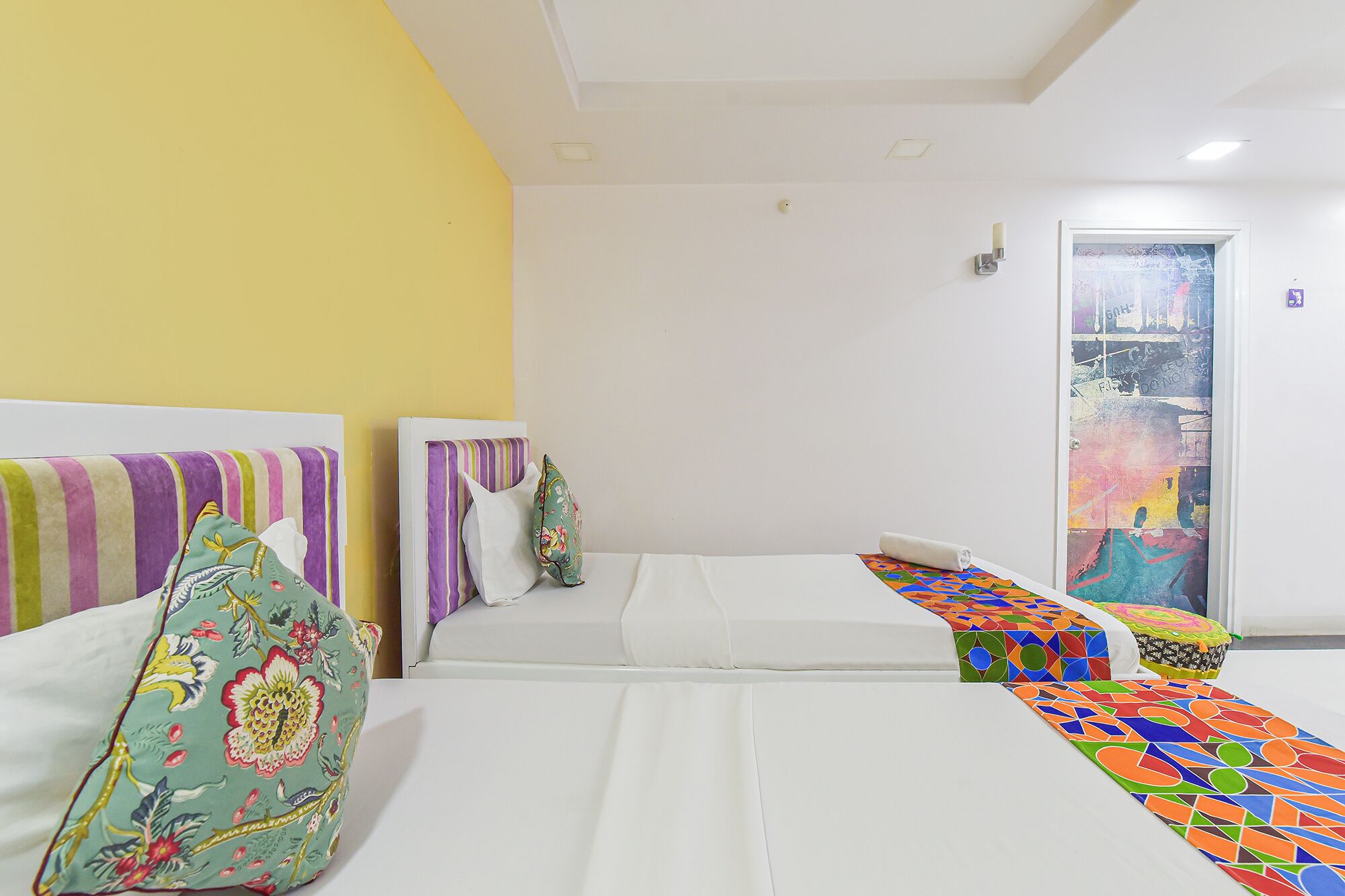 A hotel room with two beds, each with a colorful bedspread and decorative pillows.