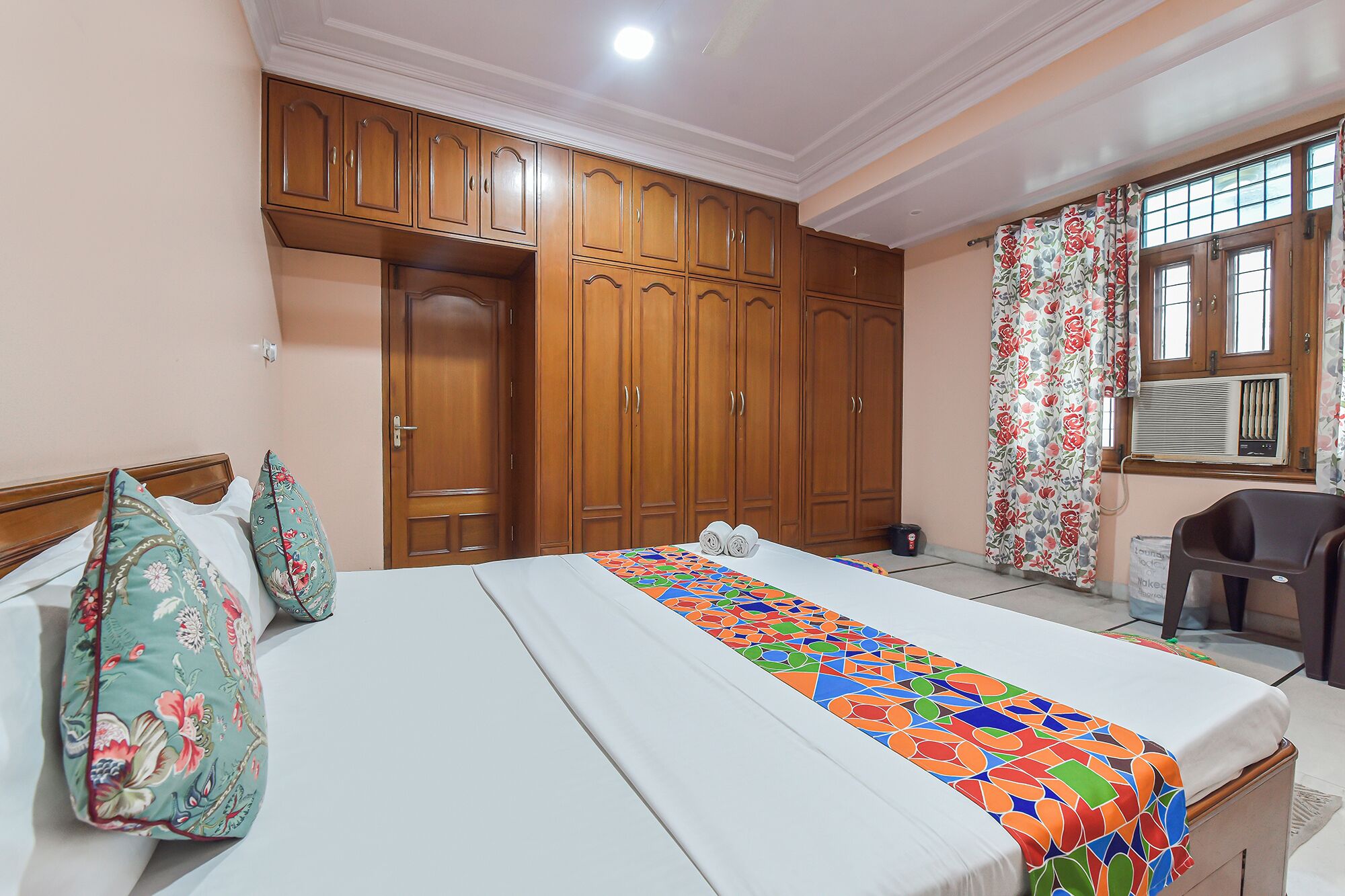 A hotel room with a bed, wooden wardrobe, and a desk with a chair.