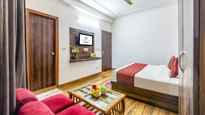 Ein Hotelzimmer mit Bett, Obst auf einem kleinen Tisch, einer Sitzecke und einem Deckenventilator, sowie einem an der Wand befestigten Fernseher.