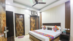 A hotel room with a bed, a nightstand, a ceiling fan, and a door. - Via Diamond Key (New Delhi)