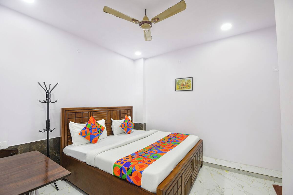 A bedroom with a bed, a ceiling fan, a coat rack, and a picture on the wall.