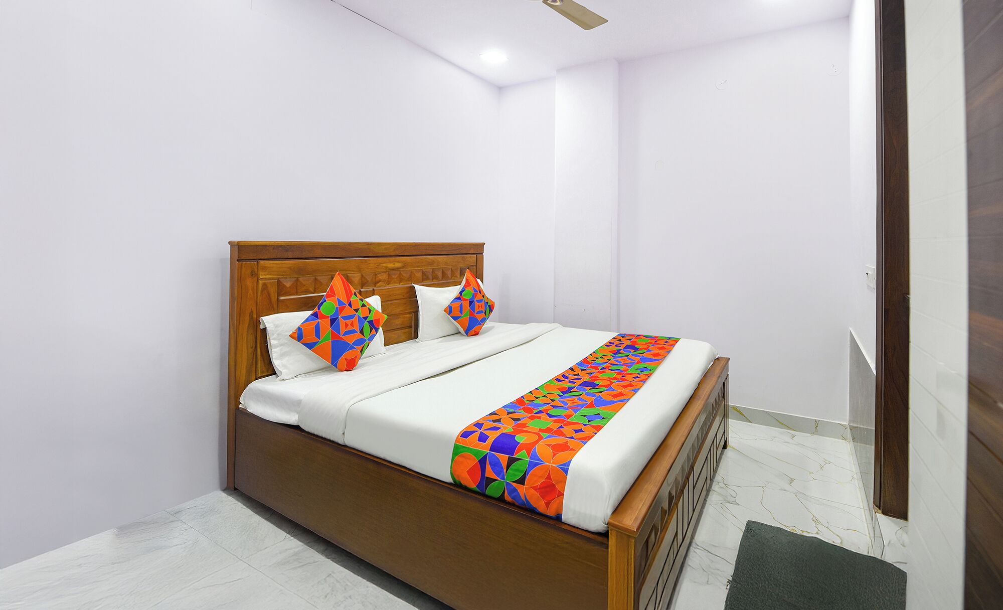 A neatly made bed with a wooden headboard, white bedding, and colorful geometric-patterned pillows and a blanket.