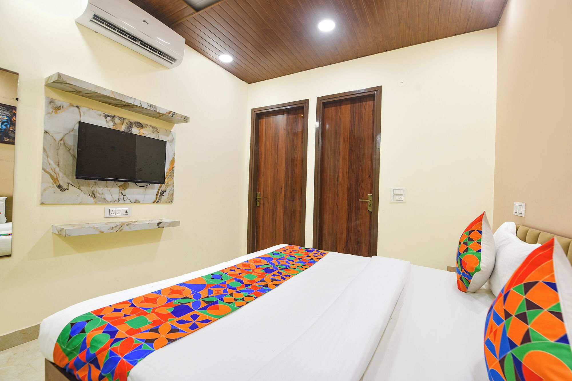 A bedroom with a bed, a TV mounted on a marble wall, wooden doors, and a ceiling with wooden beams.