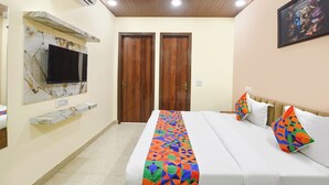 Une chambre d’hôtel avec un lit, un téléviseur fixé au mur en marbre, des portes en bois et un plafond doté d’un éclairage encastré.