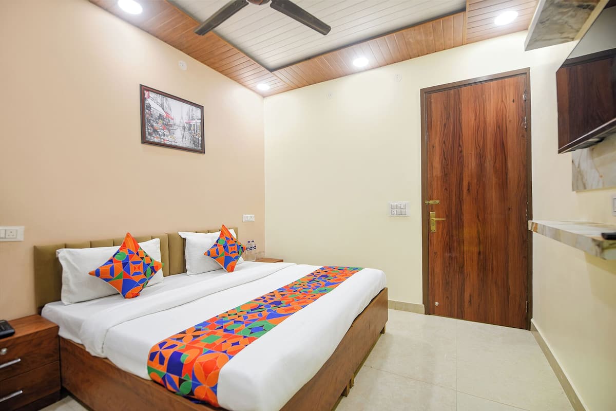 Habitación de hotel con una cama, una mesita de noche de madera, un televisor montado en la pared y una puerta.