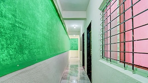 A hallway with green walls, a tiled floor, and a door with a grid pattern. - Via Pink House (Pune)