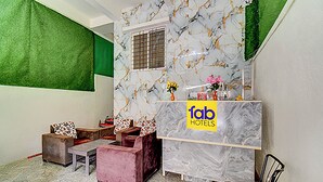 A hotel reception area with a marble wall, a reception desk, and a seating area with a sofa and chairs. - Via Pink House (Pune)
