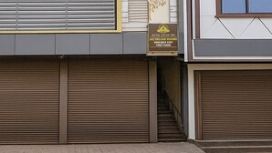 A hotel entrance with closed shutters, a sign for AJC Deluxe Rooms on the first floor, and a staircase leading inside. - Fabhotel Lotus Inn (Faridabad)