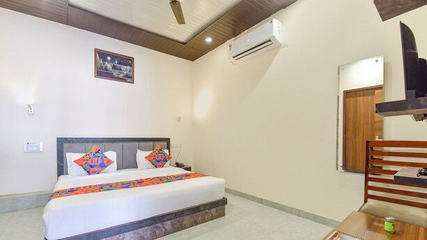 A hotel room with a bed, a nightstand, a wooden chair, a small table with a magazine, and a wall-mounted air conditioner. - Fabhotel Sunroof & Rooftop (Jaipur)