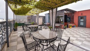 An outdoor patio with round tables and chairs, a pergola with climbing plants, and a red brick building in the background. - Fabhotel Sunroof & Rooftop (Jaipur)