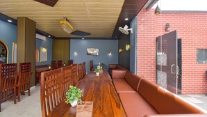 A dining area with a long wooden table, cushioned seating, and a brick wall. - Fabhotel Sunroof & Rooftop (Jaipur)
