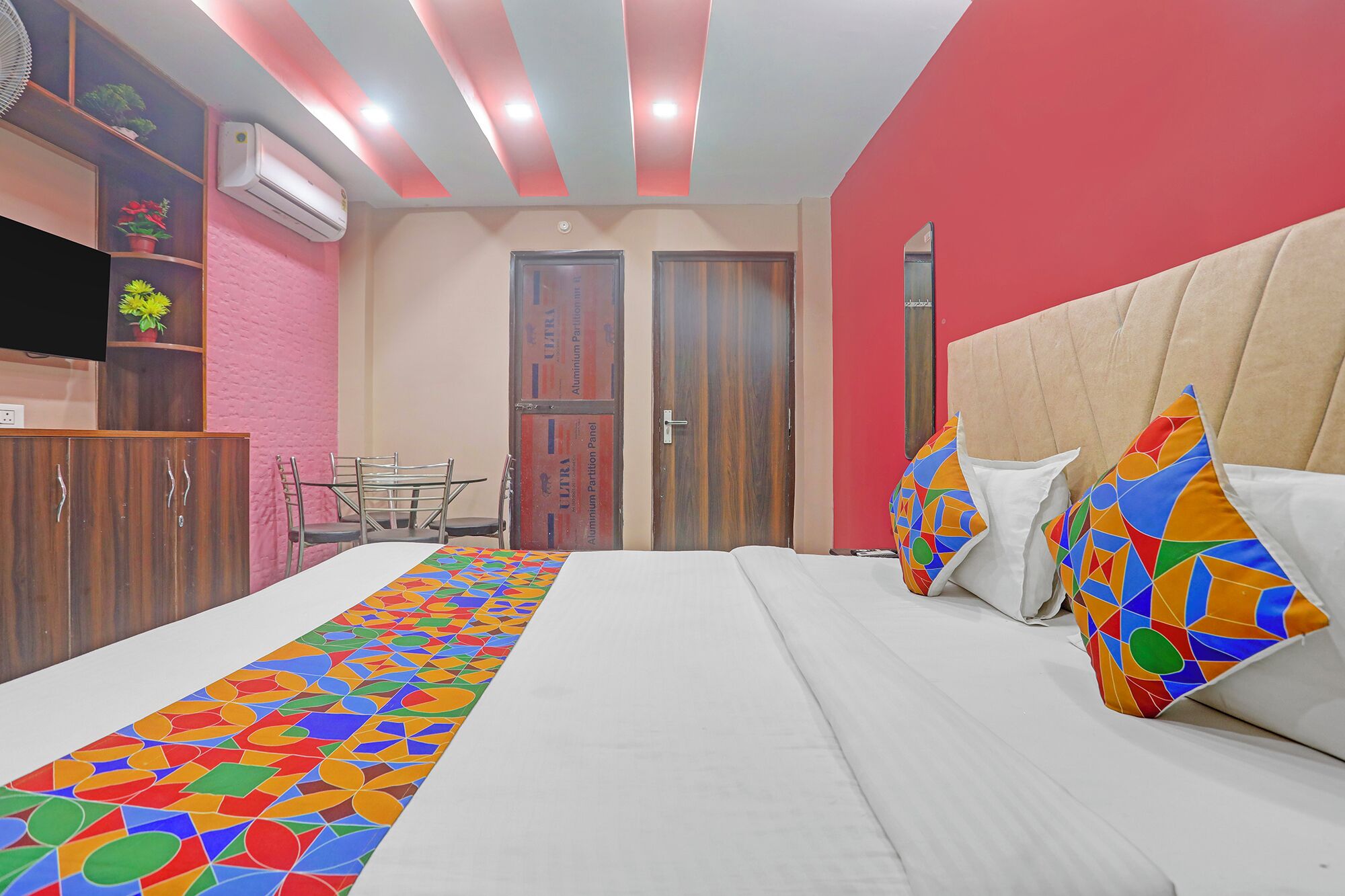 A hotel room with a bed, a desk, and a chair. There are two doors, one of which has a sign on it.