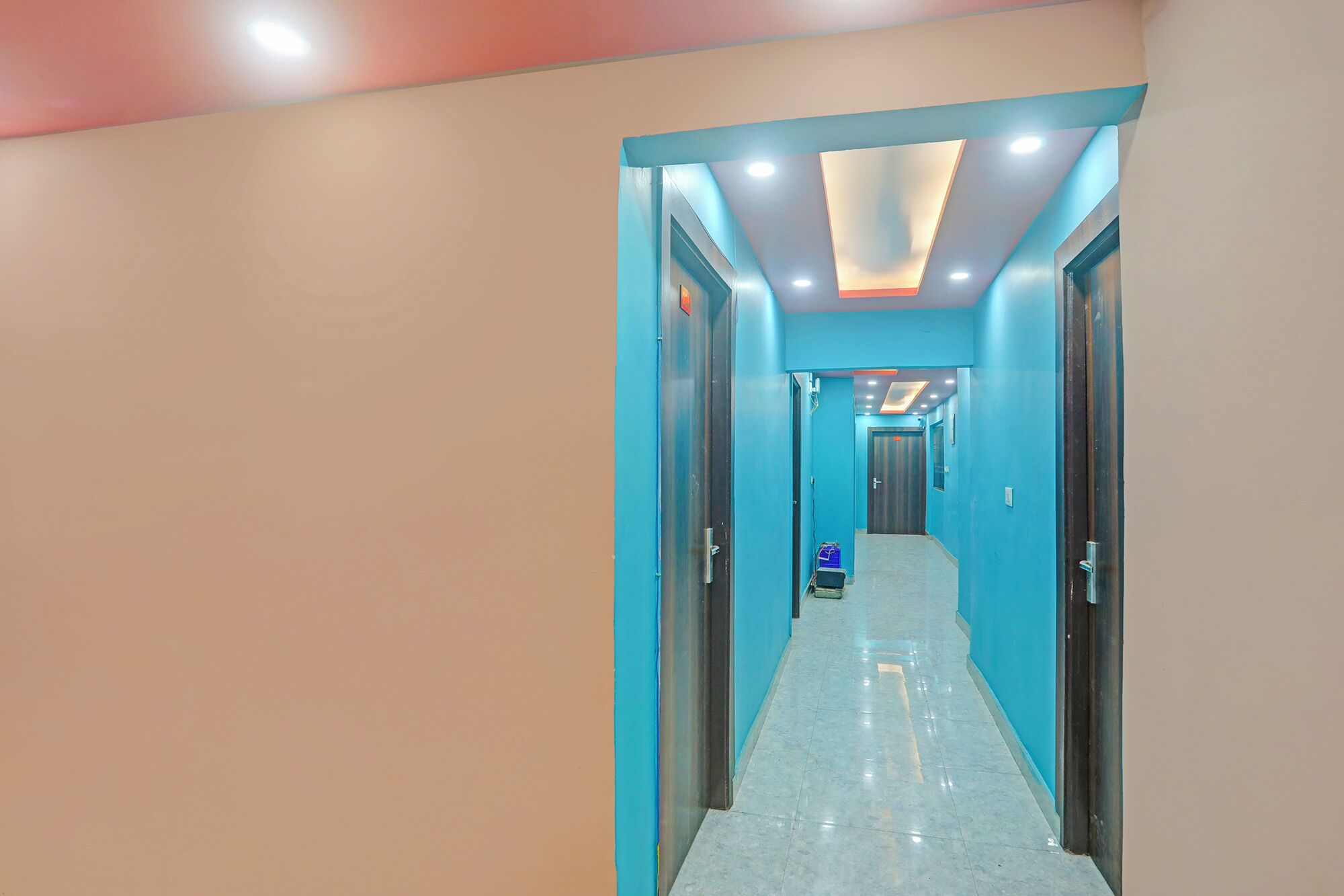 A hallway with teal walls and a white floor, leading to a room with a door.