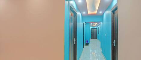 A hallway with teal walls and a white floor, leading to a room with a door.