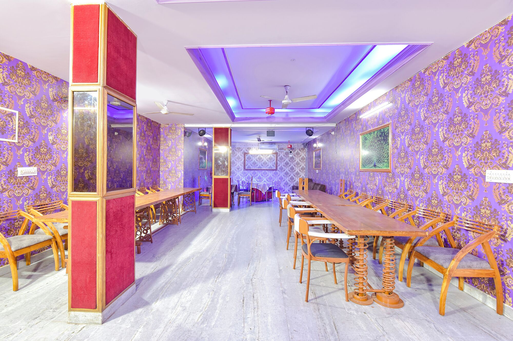 A conference room with a long wooden table and chairs, purple patterned wallpaper, and a ceiling fan.