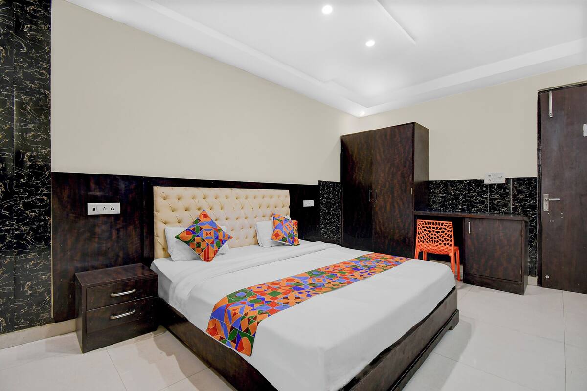 Un dormitorio moderno con una cama grande, un armario de madera oscura y una pequeña silla naranja.