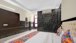 A hotel room with a large bed, a dark wood panel wall, a black marble accent wall, a ceiling-mounted air conditioner, and a window with a view. - Fabhotel Family Inn (Lucknow)