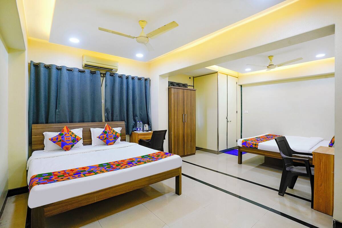 A hotel room with a large bed, a smaller bed, a desk, a chair, a wardrobe, and a ceiling fan.