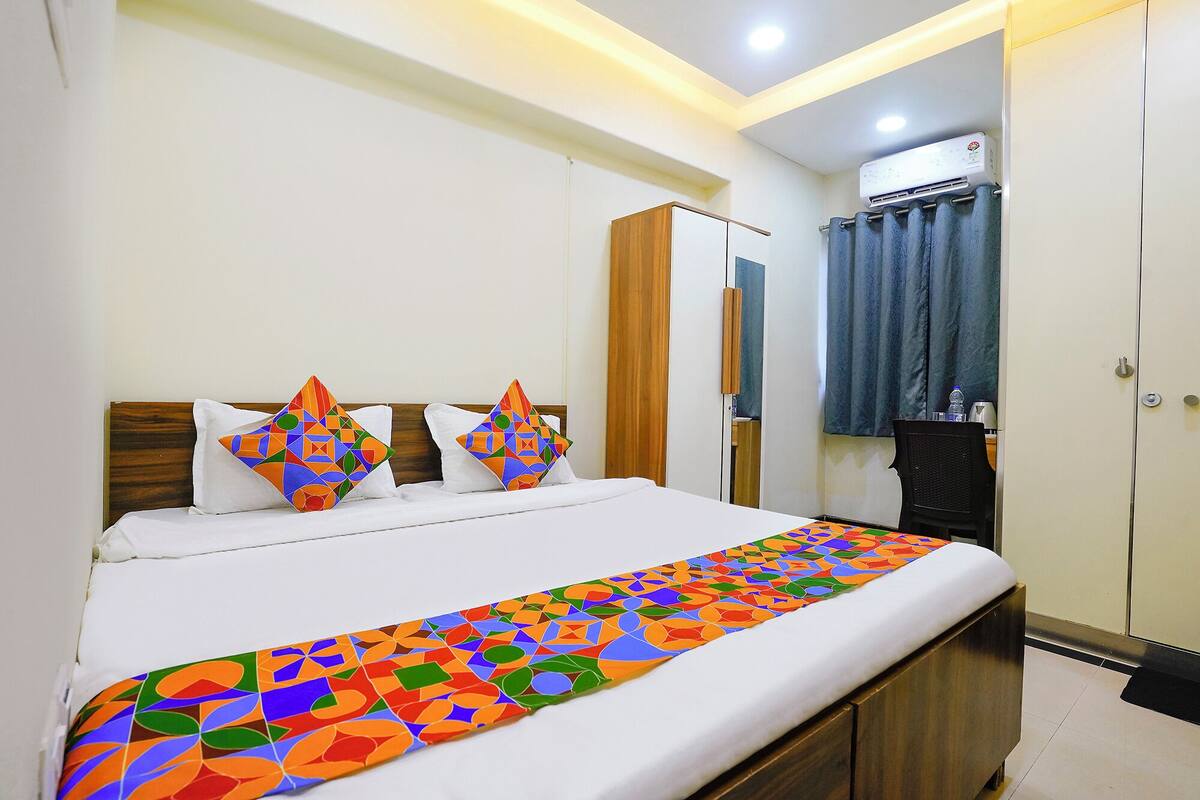 A neatly made bed with a colorful geometric-patterned bedspread, a wooden headboard, and a white pillow.