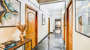 Un couloir d’hôtel avec des portes en bois, des œuvres d’art encadrées et un sol en marbre.