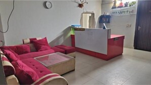 A room with a red sofa, a glass coffee table, and a reception desk. - Fabhotel Golden Palace I (Ghaziabad)