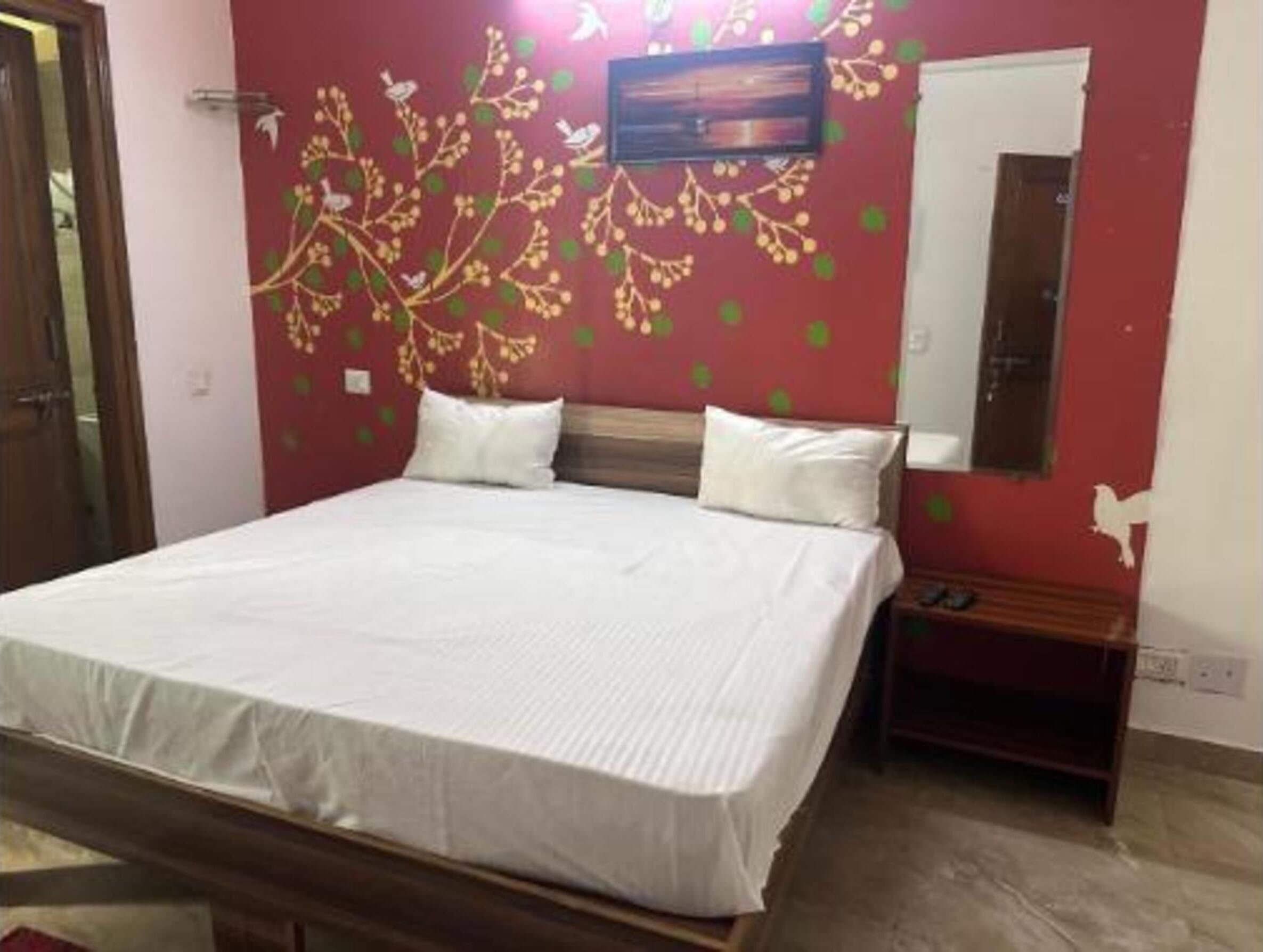 A bedroom with a bed, a TV mounted on the wall, and a small wooden nightstand.