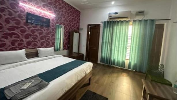 A hotel room with a bed, a desk, and a chair. There is a window with curtains, a mirror, and an air conditioning unit. - Fabhotel Golden Palace I (Ghaziabad)