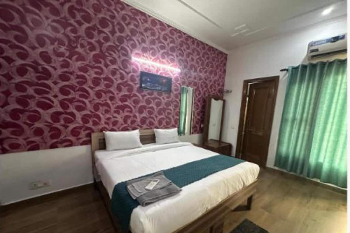 A bedroom with a bed, a nightstand, a mirror, and a window with curtains.