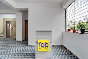 A hotel lobby with a geometric patterned floor, a reception desk, and a window with potted plants. - Fabhotel Hide Inn (Paud)