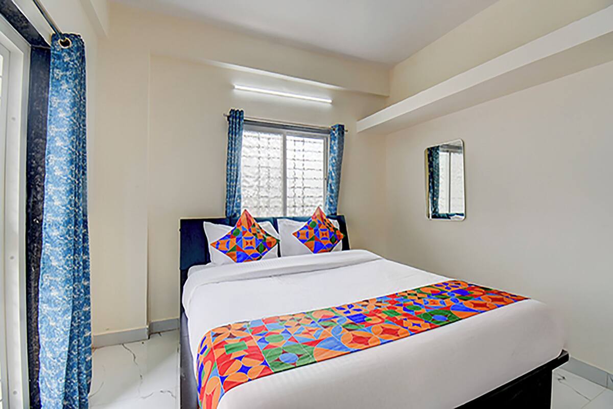 A bedroom with a bed, a window with curtains, and a wall-mounted mirror.