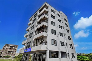 Un hotel de varios pisos con balcones, un letrero que dice 'Fab Hotels' y un cielo azul despejado.