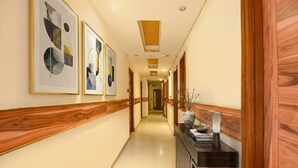 A hallway with framed abstract art on the walls, a wooden panel design, and a reception desk with a vase and lamp. - Fabhotel Atithi (New Delhi)