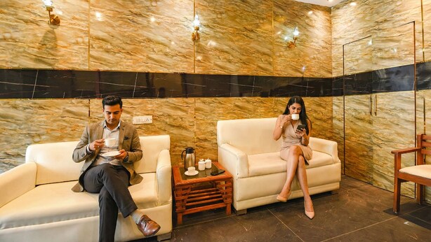 A modern interior with marble walls, two sofas, a wooden side table, and a mirror. - Fabhotel Atithi (New Delhi)