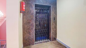 An elevator with a metal gate, a fire extinguisher mounted on the wall, and a textured wall. - Fabhotel Avante Palace (Ranchi)