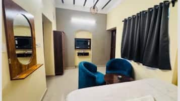 A hotel room with a bed, a blue armchair, a wooden wardrobe, a mirror, and a ceiling fan.
