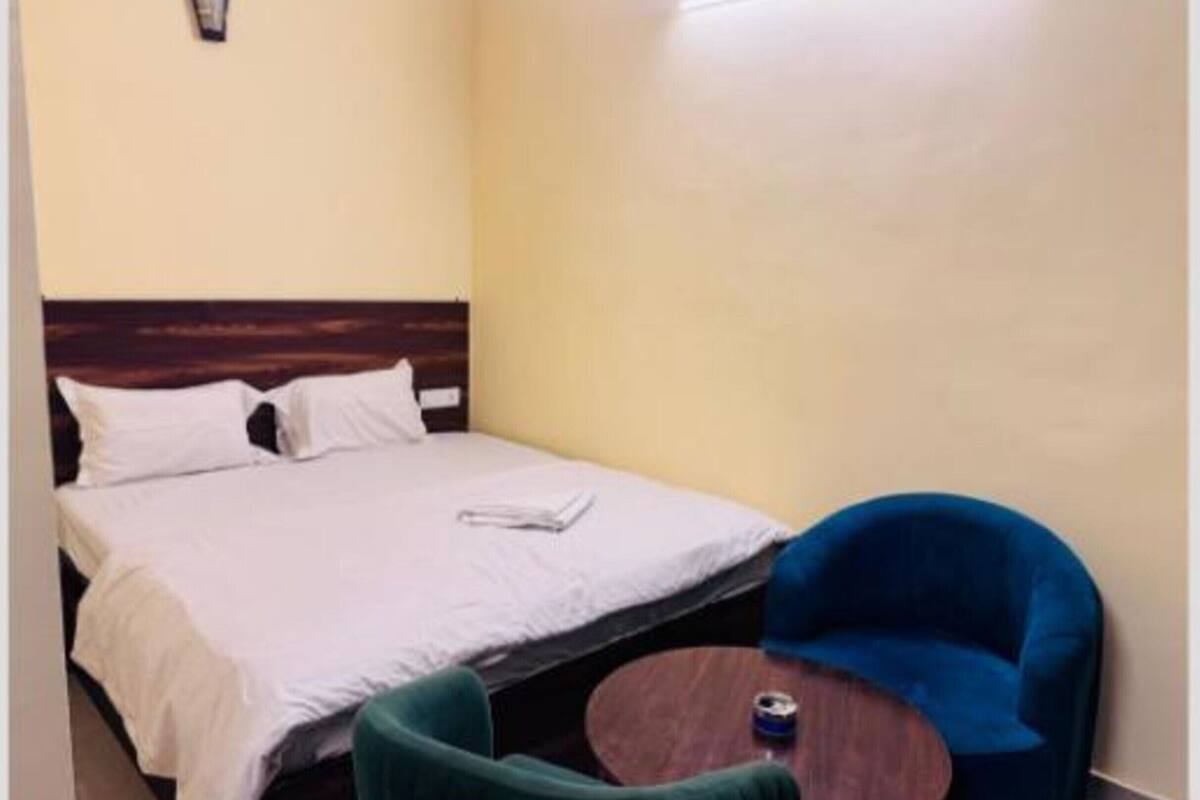 A single bed with white bedding, a green armchair, and a small round table with a cup.