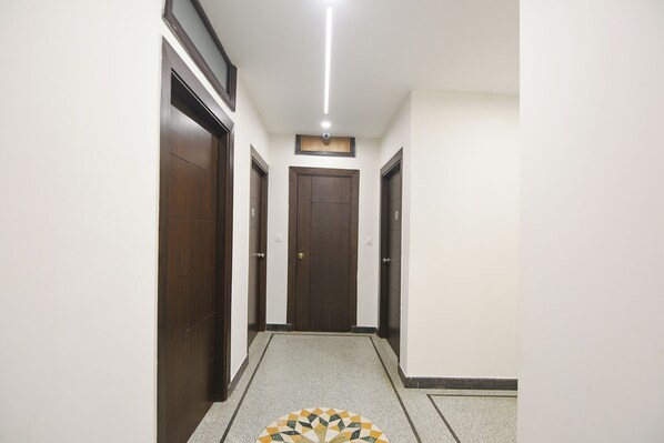 A hallway with three wooden doors, a tiled floor, and a ceiling light. - Fabhotel Sai Village (Gurugram)