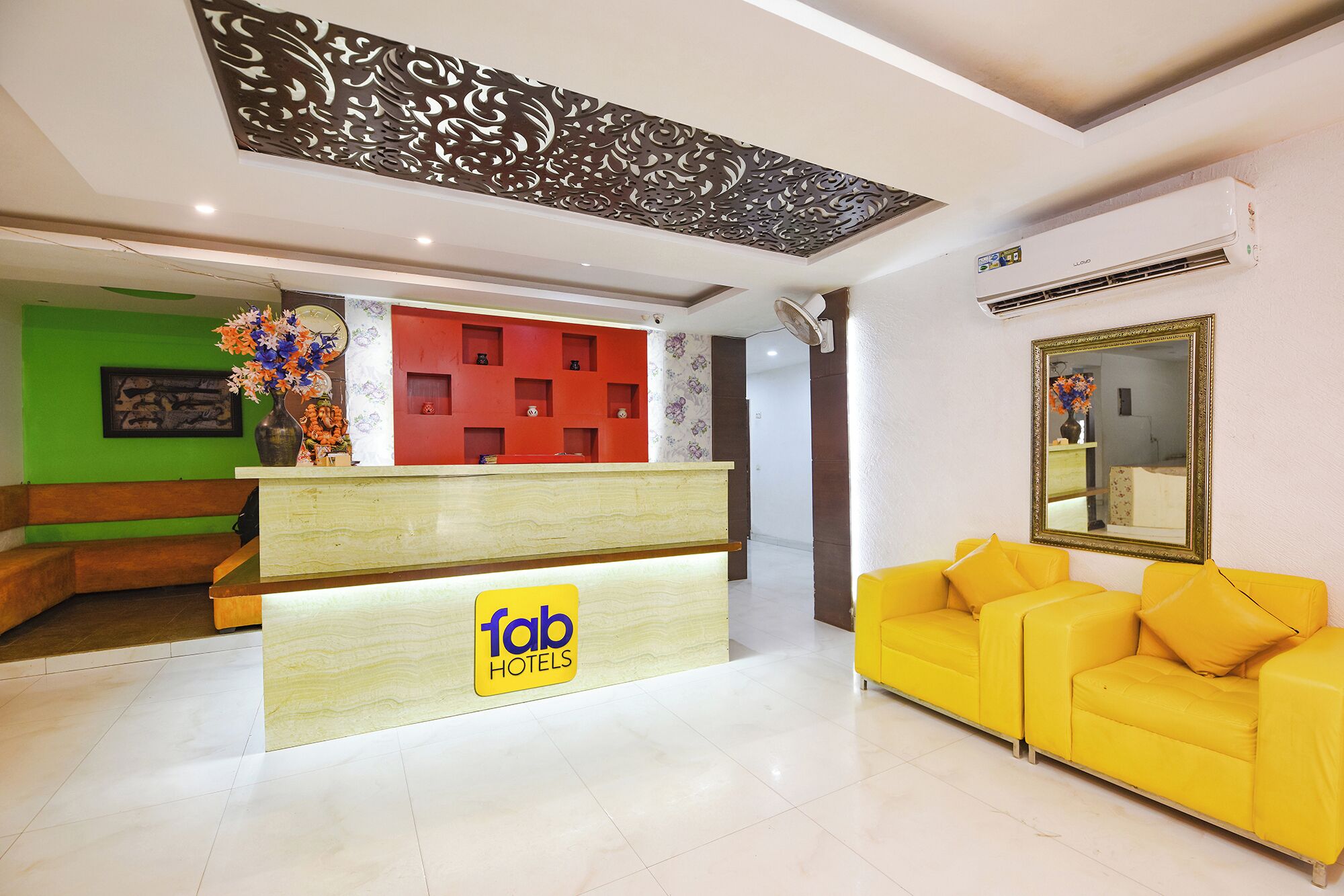 Zona de recepción de hotel con diseño moderno, que incluye un mostrador de recepción, un sofá amarillo y un techo decorativo.