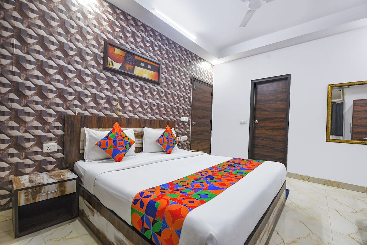A hotel room with a geometric patterned wall, a bed with white linens, colorful pillows, a wooden headboard, a bedside table, and a mirror on the wall.