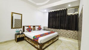 A bedroom with a bed, a nightstand, a mirror, and a window with curtains. - Fabhotel Clayton (New Delhi)