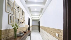 A hallway with a reception desk, framed artwork on the wall, and a staircase in the distance. - Fabhotel Clayton (New Delhi)