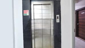 An elevator with a metallic interior, a red emergency sign, and a door with a "Administration" label. - Fabhotel Clayton (New Delhi)