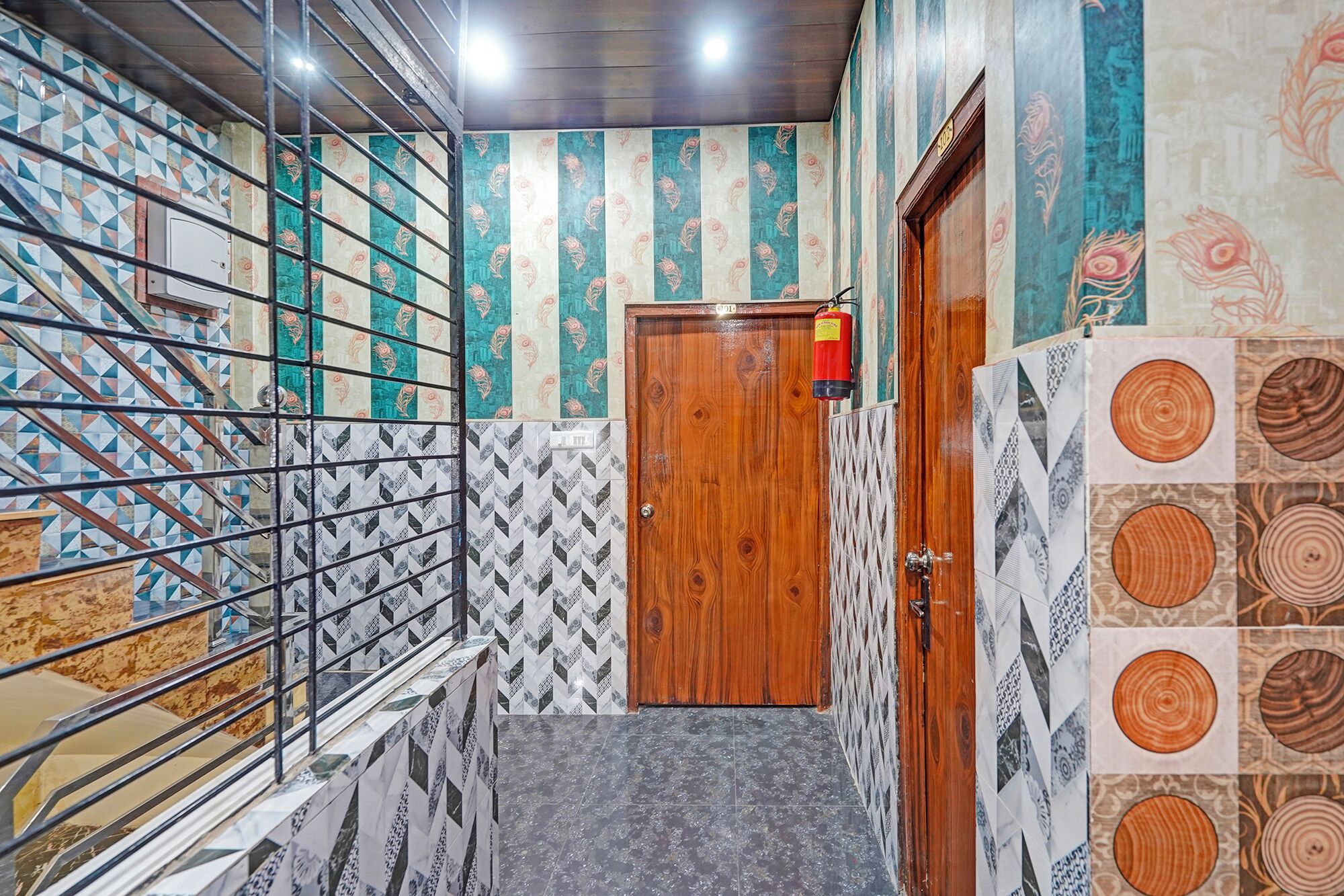A hallway with a wooden door, a fire extinguisher, patterned walls, and a metal railing.