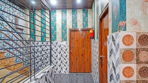 A hallway with a wooden door, a fire extinguisher, patterned walls, and a metal railing. - Via Ayodhya Residency (Ayodhya)
