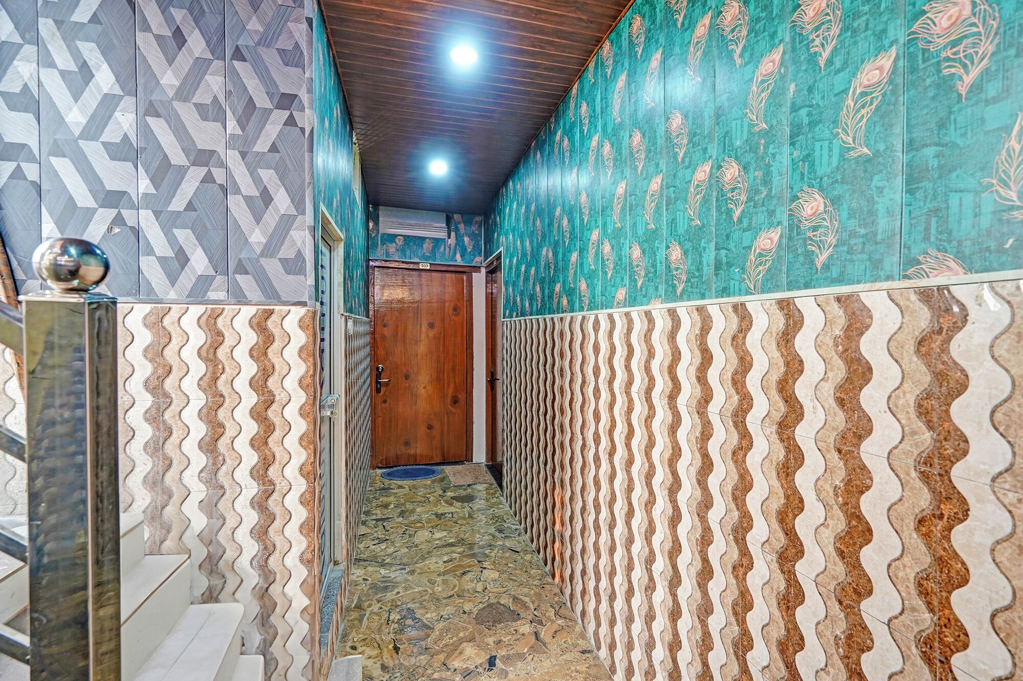 A narrow hallway with patterned walls and a tiled floor, leading to a wooden door.