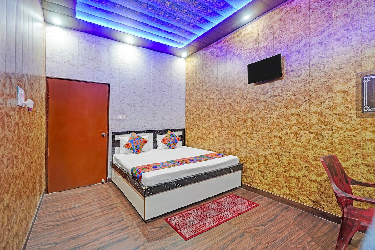 Une chambre d’hôtel avec un lit, un fauteuil rouge, un mur en bois à texture marquée et un plafond éclairé de lumière bleue.
